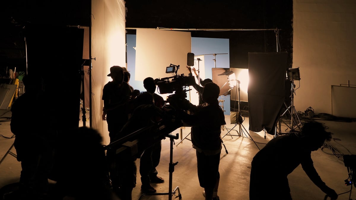 Silhouette of a film crew and camera on a dolly crane beneath studio lights