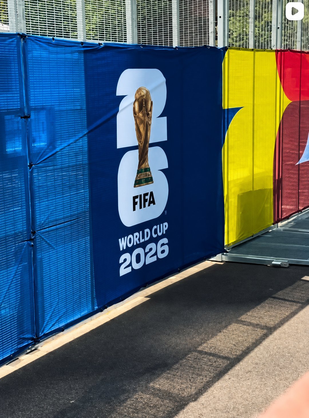 FIFA World Cup 2026 promotional banner with trophy logo on blue panel, flanked by yellow and red colored panels