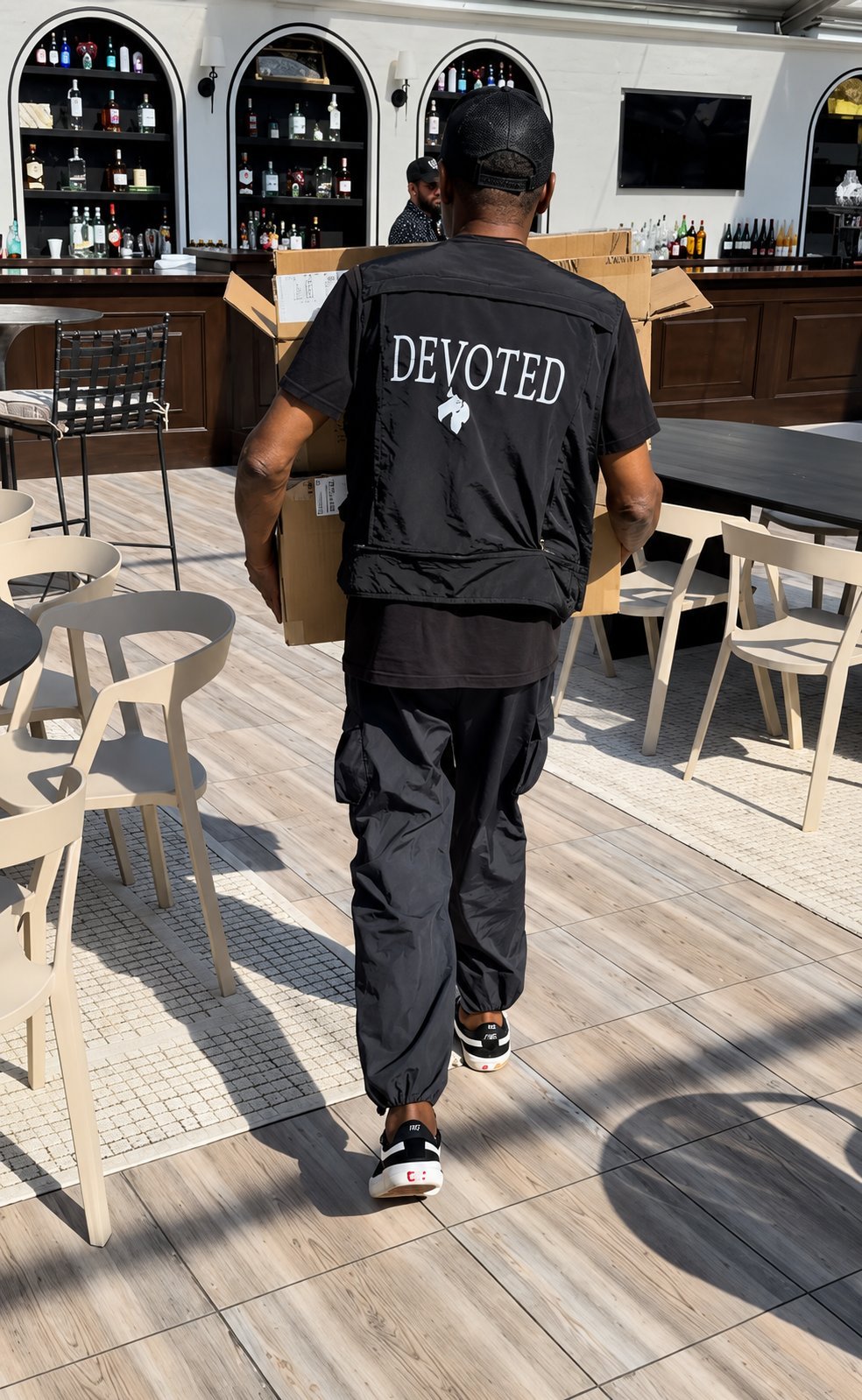 Person wearing black DEVOTED outfit running through a modern bar interior with arched shelving and wooden furniture